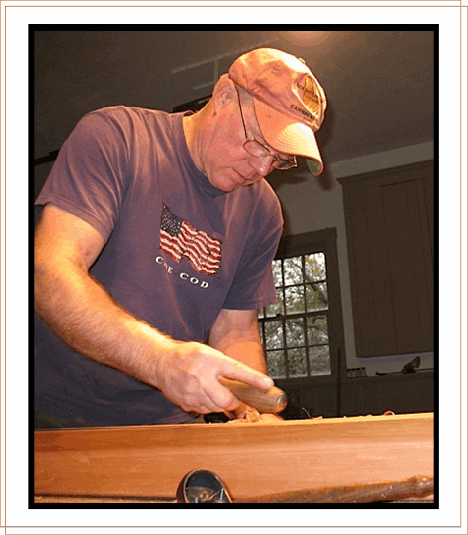 Man sanding wood indoors, wearing a cap and a casual T-shirt.