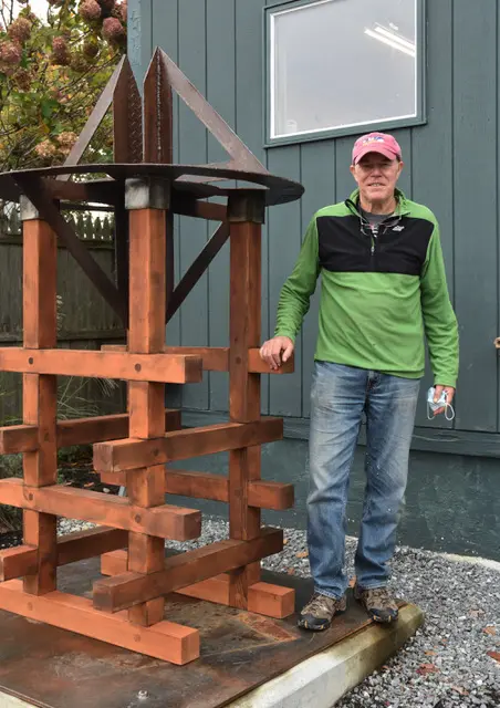 Man in casual clothes standing by a wooden structure outdoors.