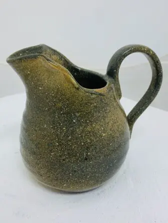 A rustic, brown ceramic pitcher with a curved handle and spout.