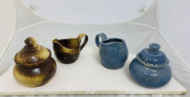 Four small ceramic pitchers in brown and blue on a white surface.