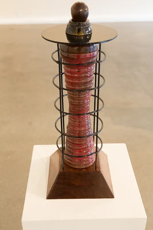 A tall, spiraled sculpture with red and pink hues encased in metal rings on a wooden base.