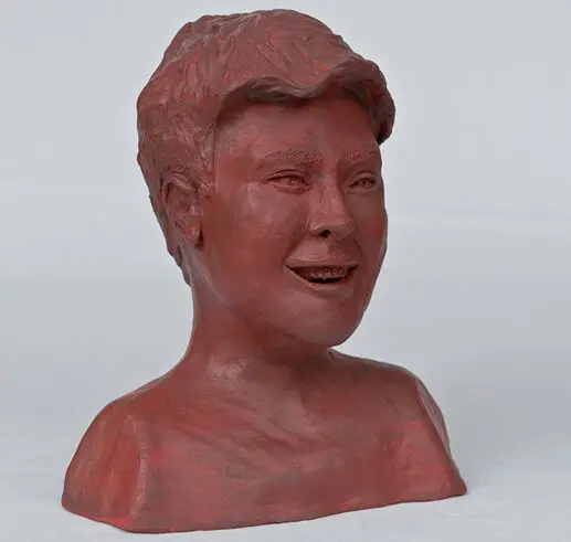 A clay bust sculpture of a smiling man with styled hair.
