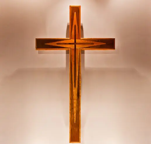 A wooden cross illuminated against a soft beige background.