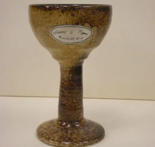 A rustic ceramic chalice with a textured finish and a label on its bowl.