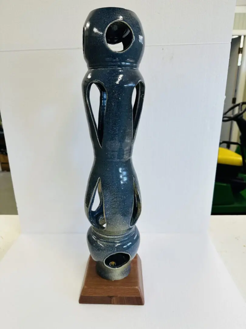 Tall ceramic sculpture with abstract human features and a hollow base.