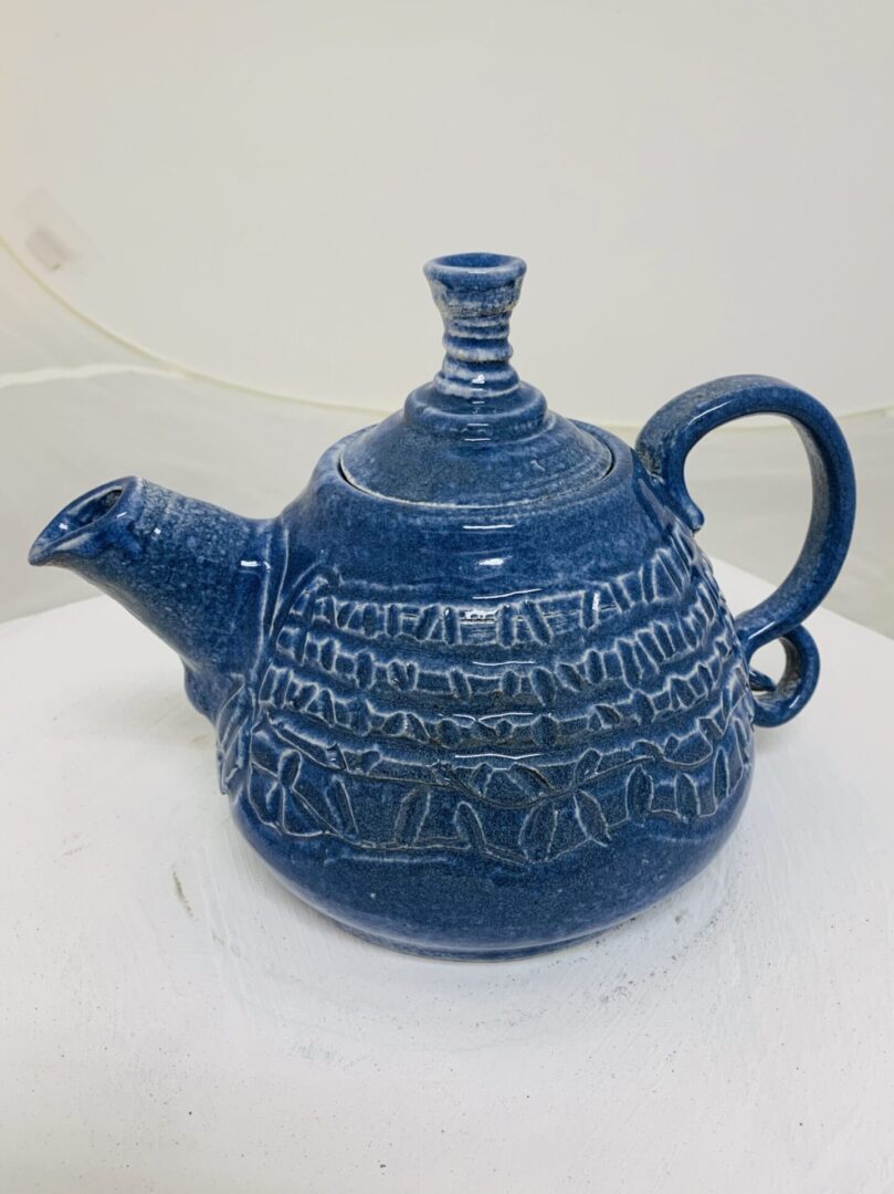 Blue ceramic teapot with intricate textured design and a spout shaped like an animal's head.