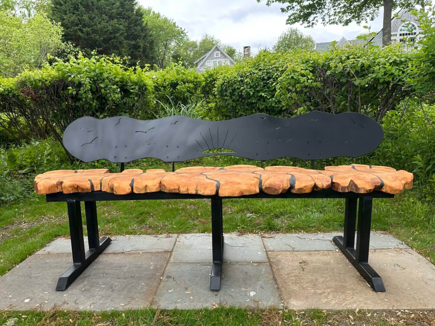 Unique bench with a top that mimics a wooden plank and a black backrest shaped like a cloud.