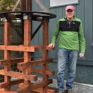 Man in casual clothes standing by a wooden structure outdoors.