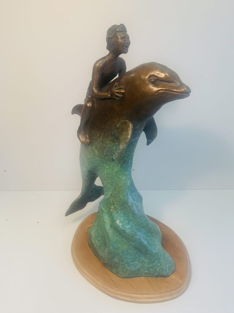 Bronze sculpture of a child riding a dolphin on a wave.