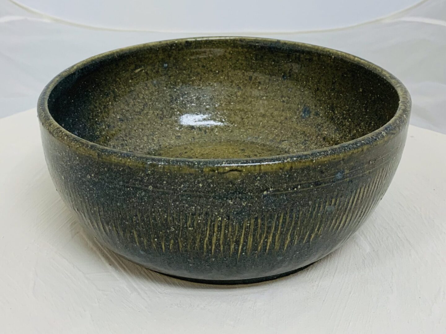 A rustic, dark green ceramic bowl with textured vertical lines.