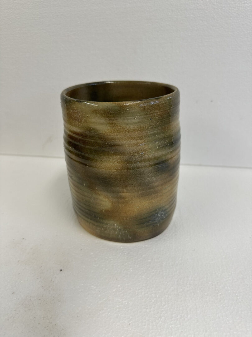 A small ceramic cup with earthy brown and green glaze.