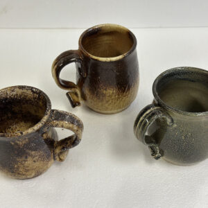 Three handmade pottery mugs with unique textures and earthy tones.