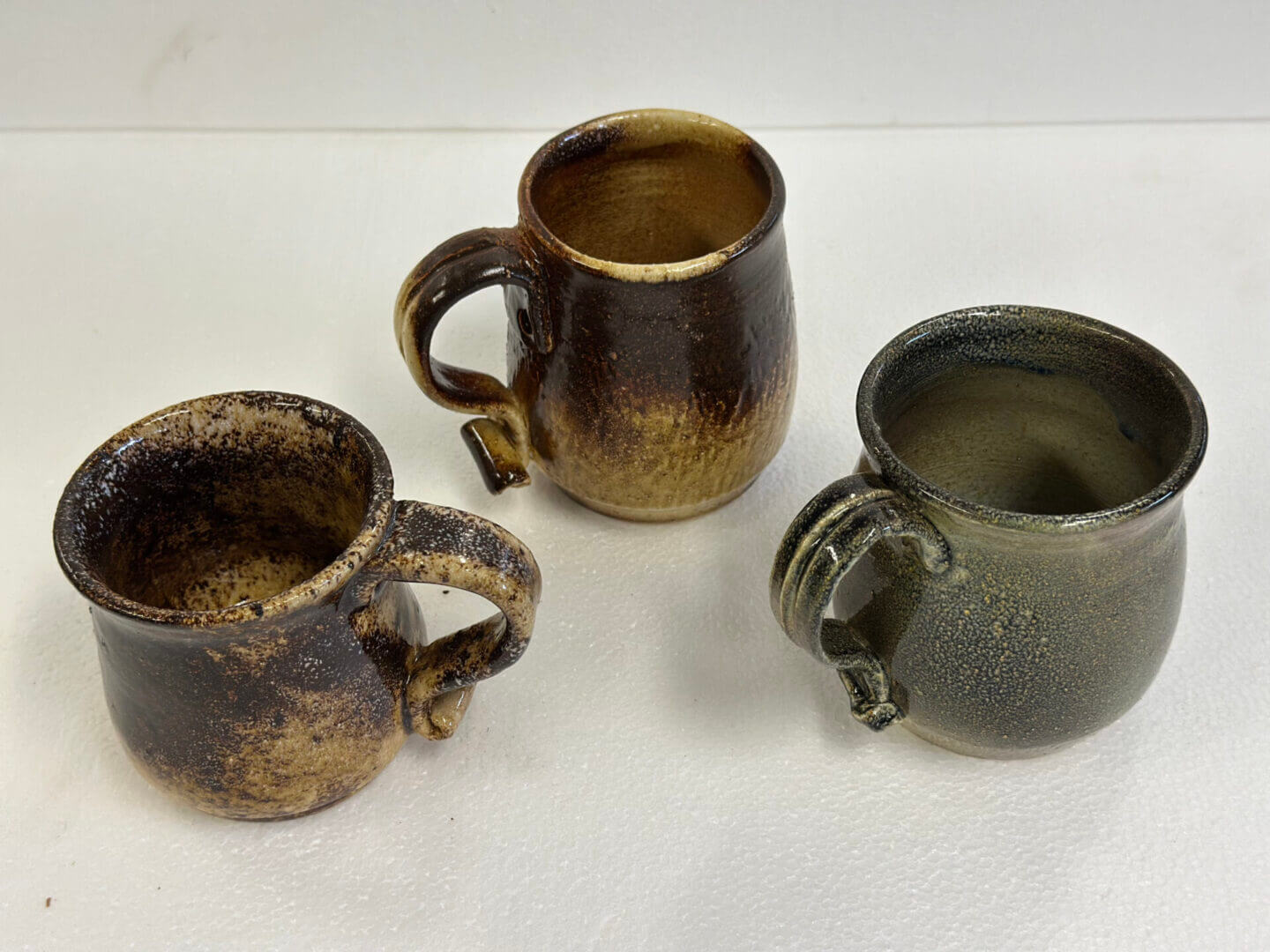 Three handmade pottery mugs with unique textures and earthy tones.