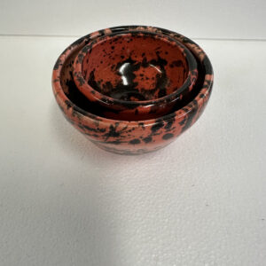 Round black and red speckled container with lid on white surface.