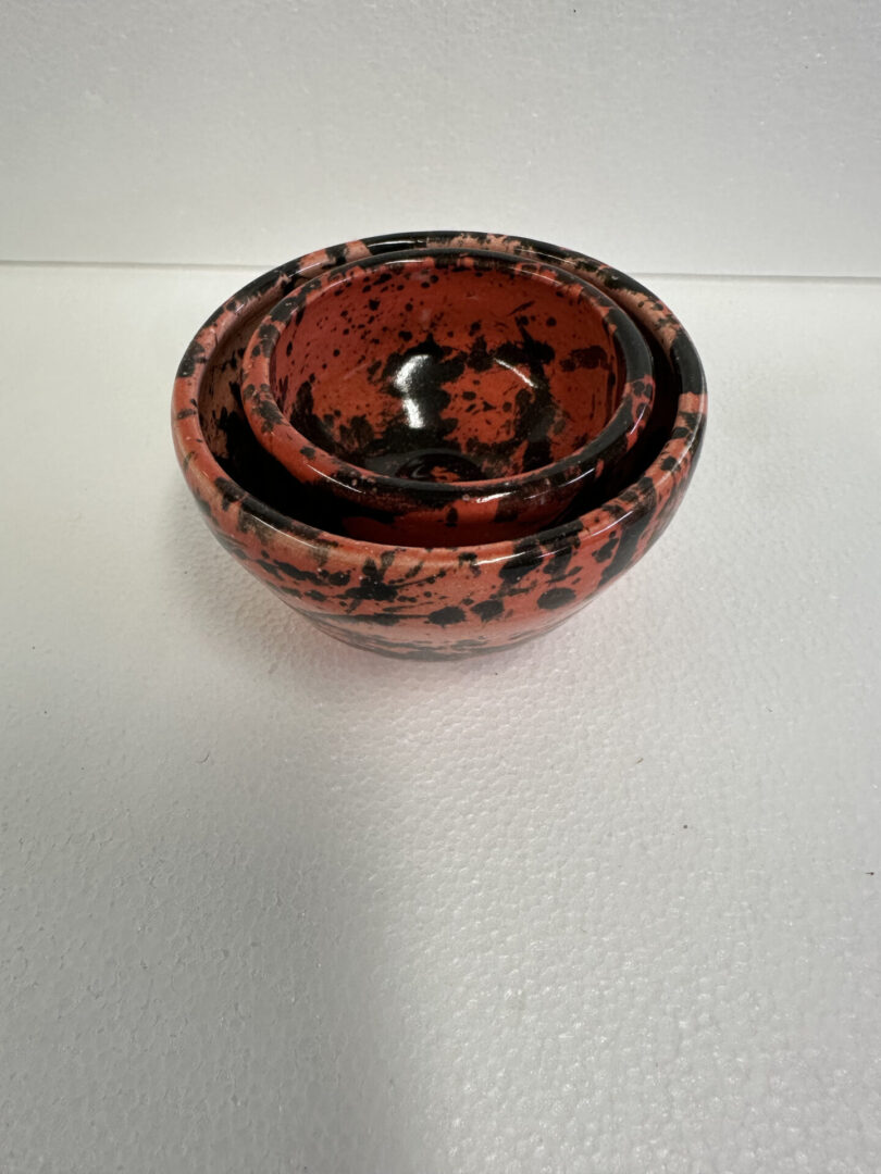 Round black and red speckled container with lid on white surface.