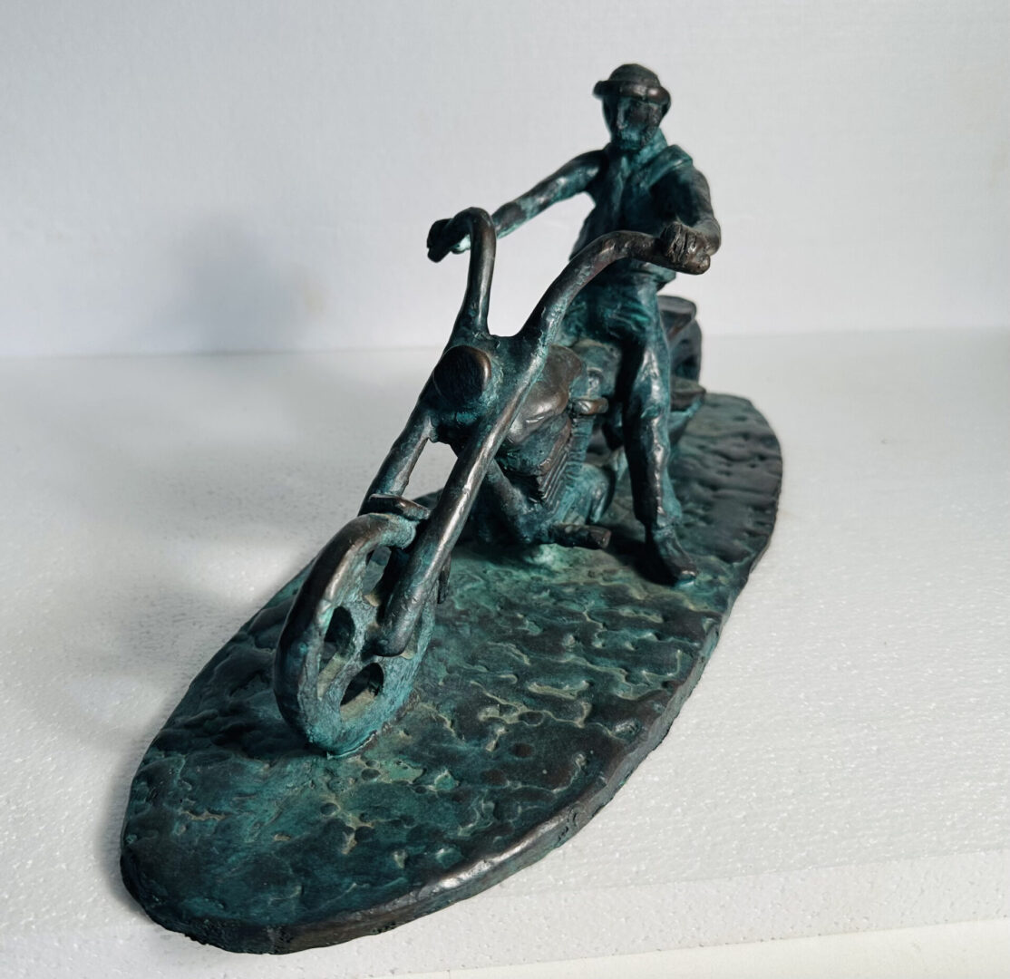 Bronze sculpture of a person riding a chopper-style bicycle.