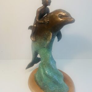 Bronze sculpture of a child riding a dolphin on a wave.