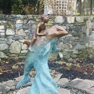 A child statue riding a dolphin sculpture near a stone wall.
