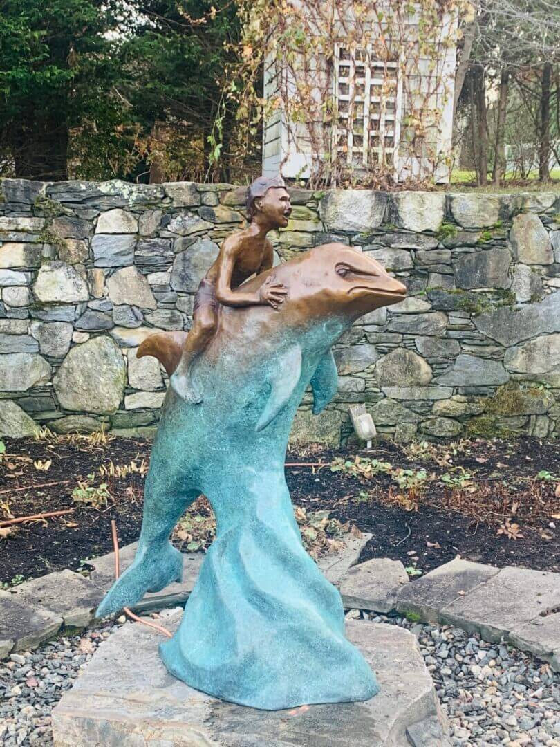 A child statue riding a dolphin sculpture near a stone wall.