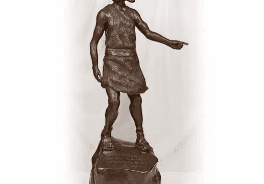 Bronze statue of a man pointing forward while standing on a rock.