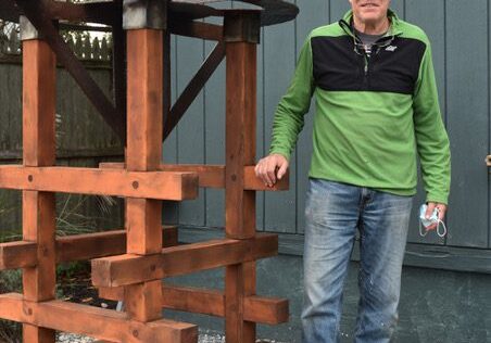 Man in casual clothes standing by a wooden structure outdoors.